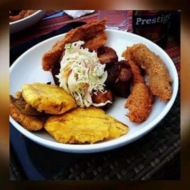 A plate of fried fish, plantains, coleslaw, and crispy chicken.